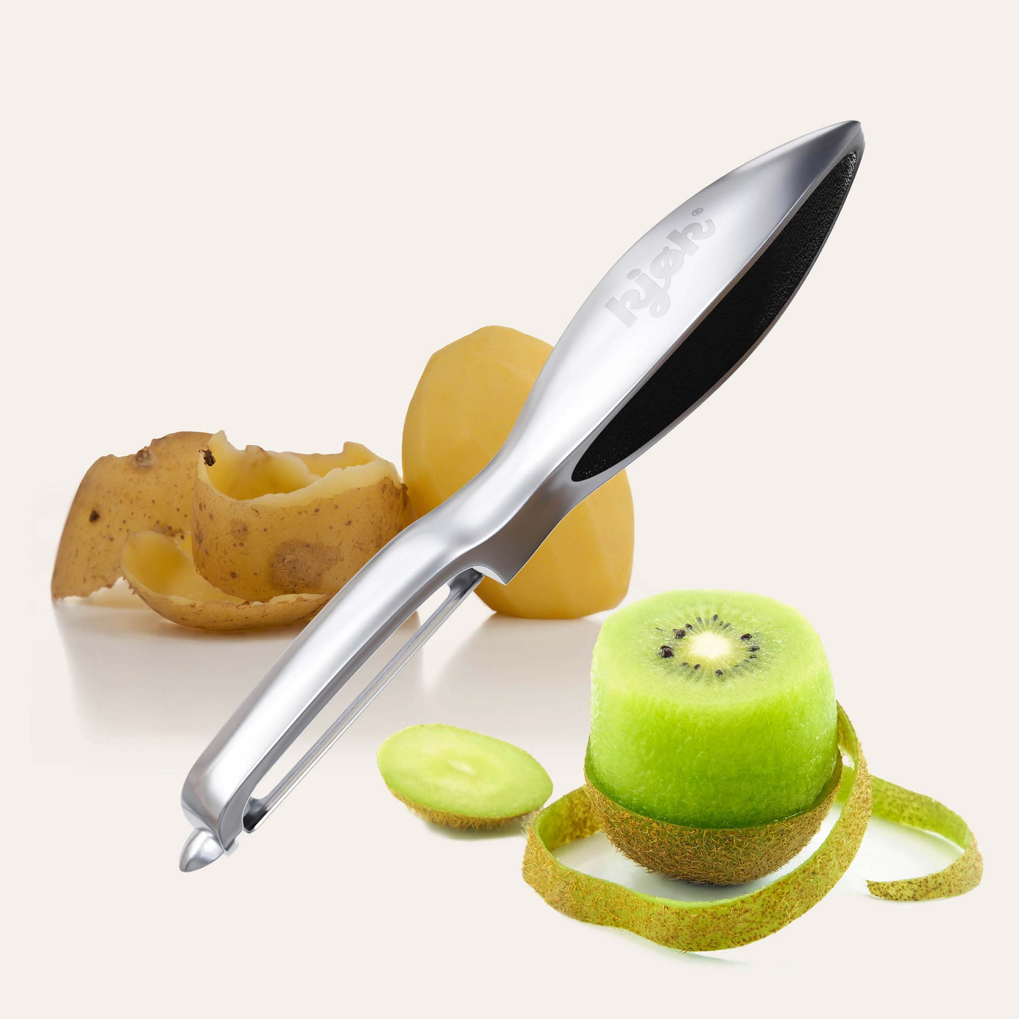 Sparschäler von kjøk, dahinter geschälte Kartoffel mit Schale nebenan und halb geschälte Kiwi im Vordergrund