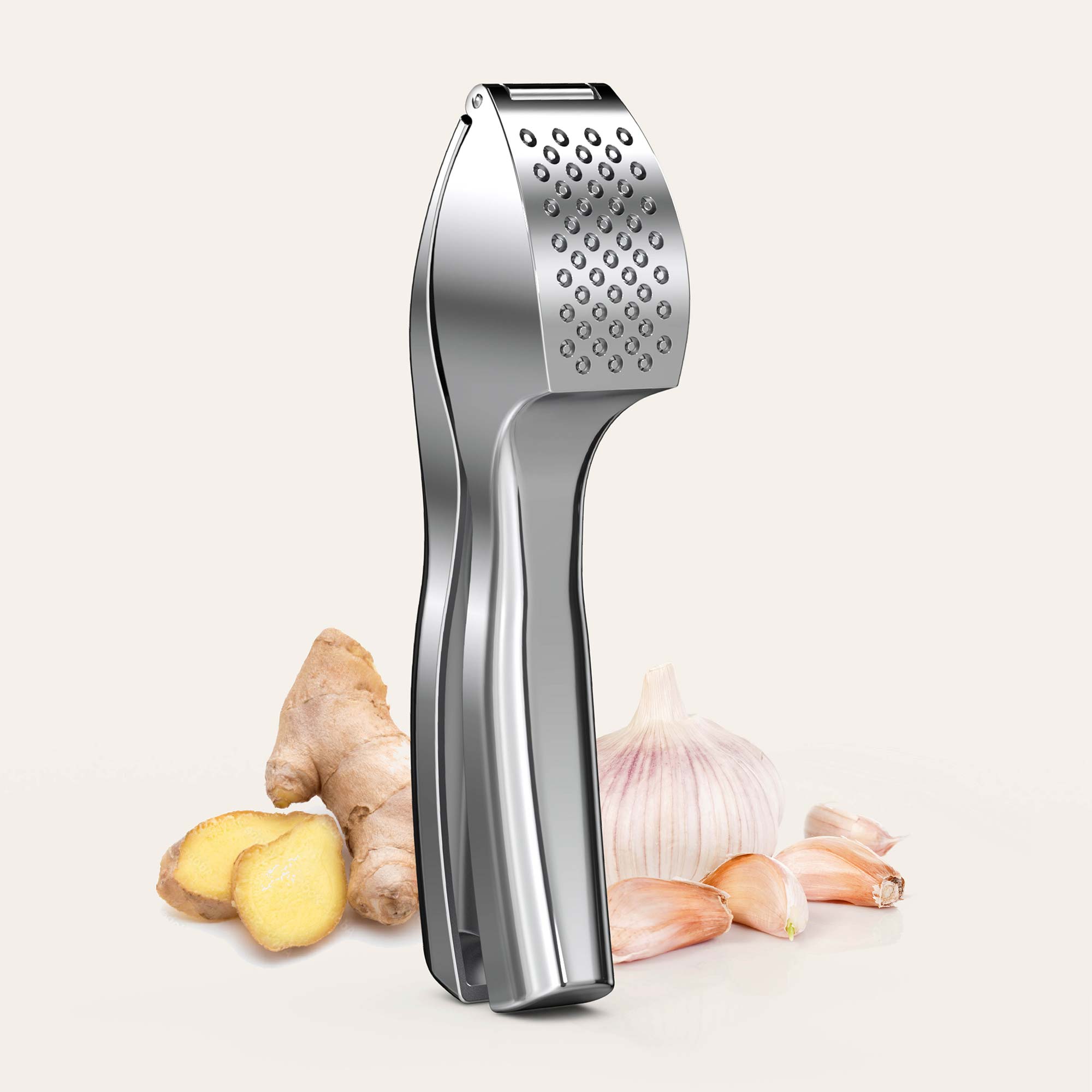 Silberne Knoblauchpresse vor Knoblauch und Ingwer auf hellem Hintergrund