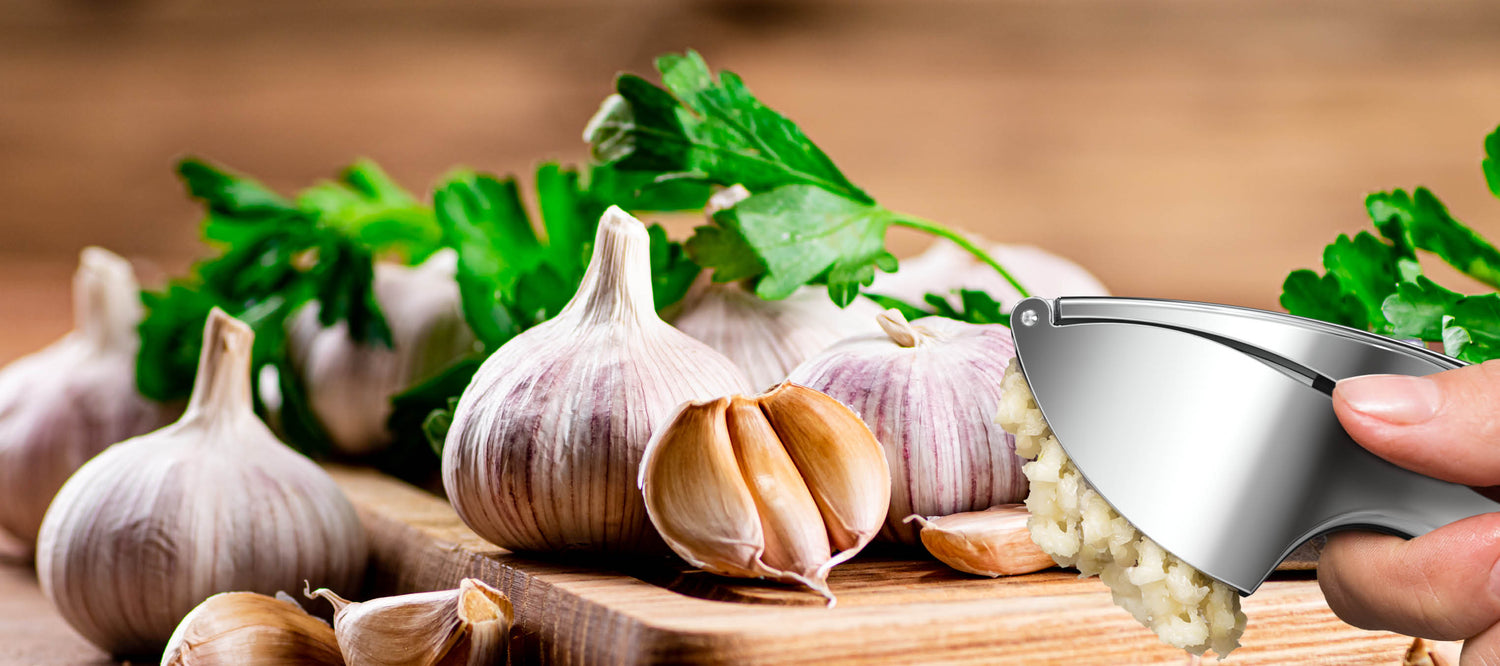 Frische Knoblauchknollen mit Knoblauchpresse von kjøk beim Pressen auf Holzunterlage