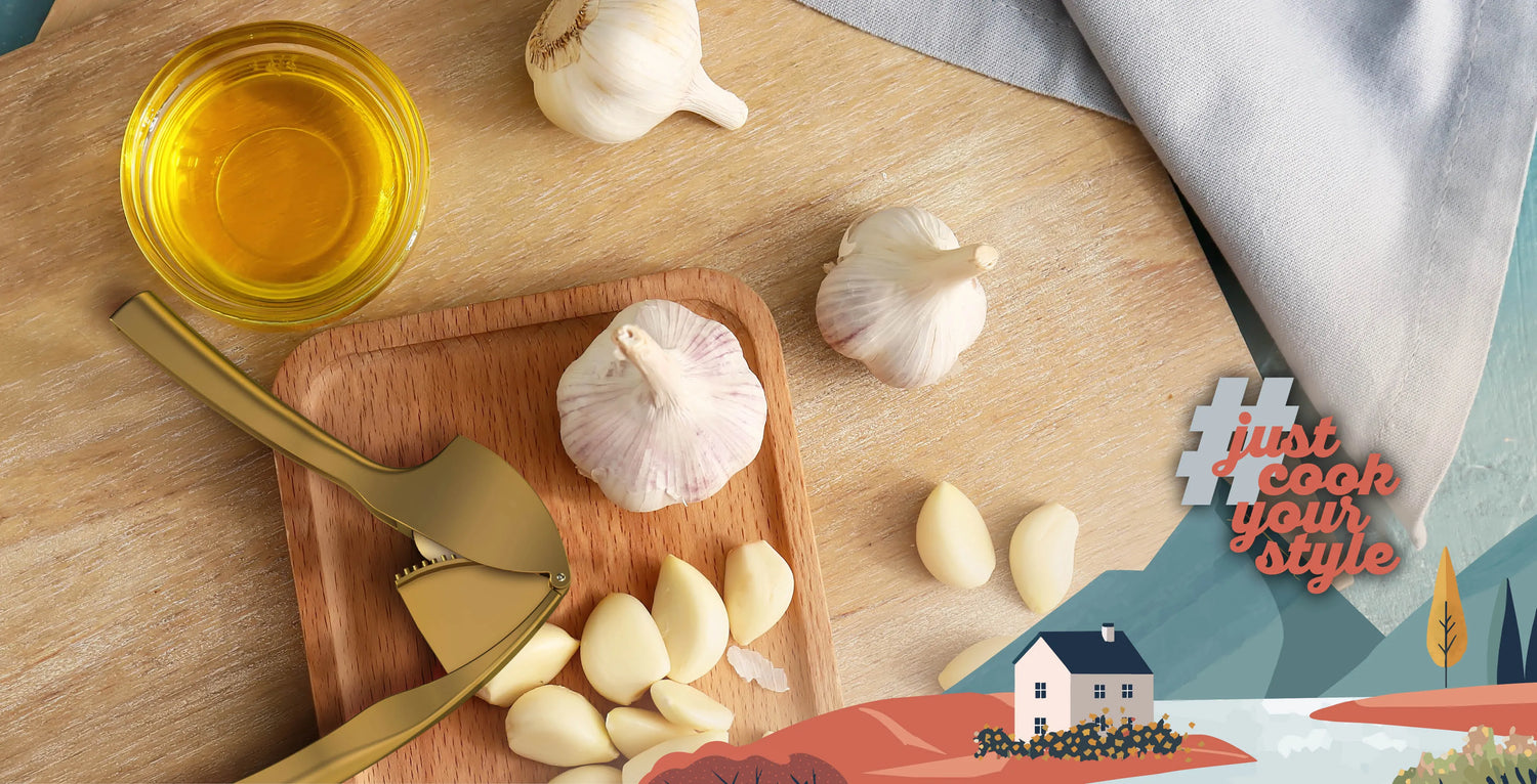 kjøk Knoblauchpresse in Gold auf Schneidebrett mit frischem Knoblauch und Olivenöl – praktisches Küchenwerkzeug für aromatische Gerichte mit #justcookyourstyle
